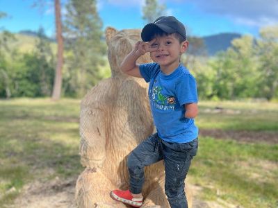 Braeson is posing on the statue of a bear made out of wood.